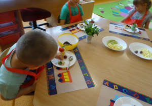 Dzieci dekorują lody w wafelku owocami.